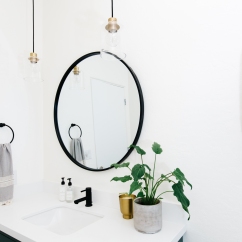 white bathroom walls with black circle mirror, brass and glass pendant lights