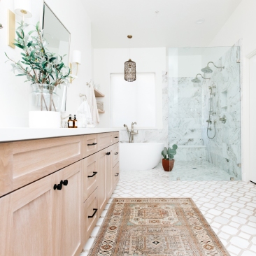 master bathroom double vanity in oak with tribal print rug and marble tile and soaker tub