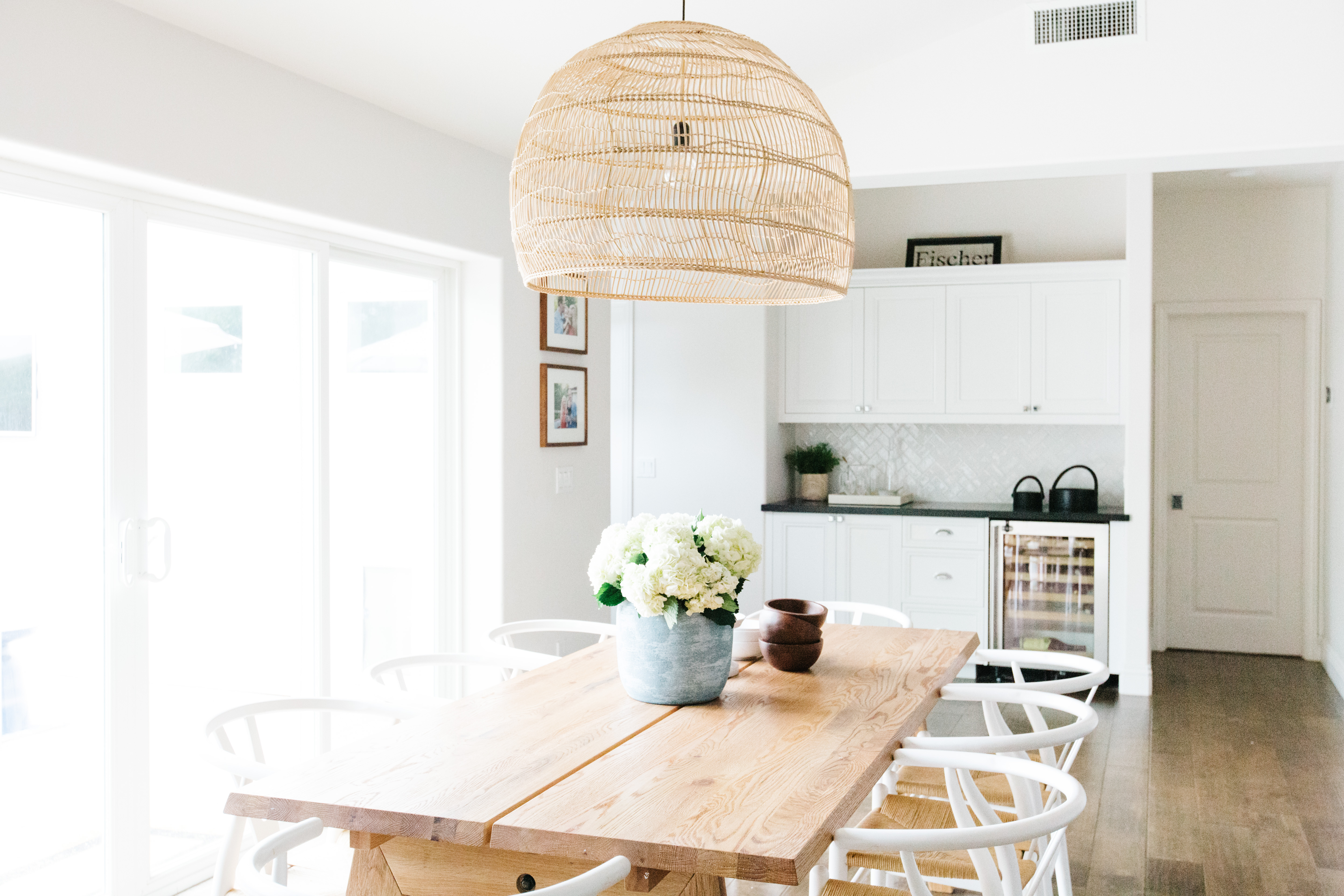 modern wicker light fixture over natural wood table and white chairs